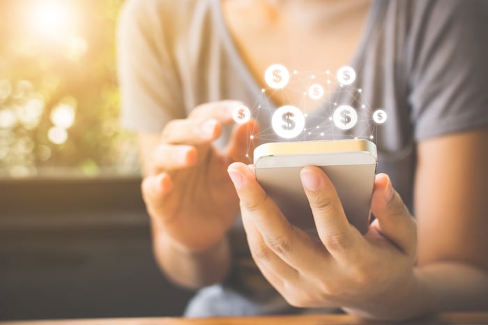 Woman using smartphone with dollar signs floating over it