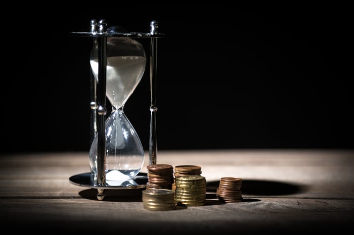 Several coin stacks around the base of a large hourglass.