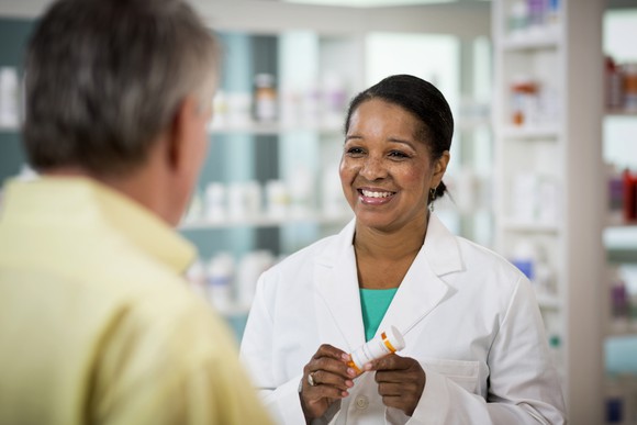 A smiling pharmacist holding a prescription bottle while consulting with a customer.