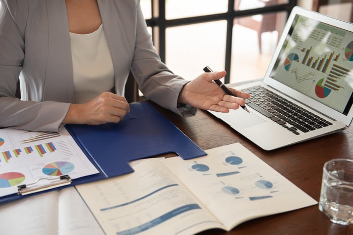 Woman at desk with laptop and documents with graphs in front of her