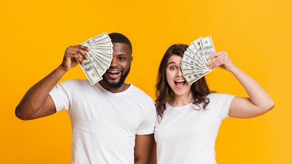 Young man and woman in white tee shirts holding cash in front of their faces.