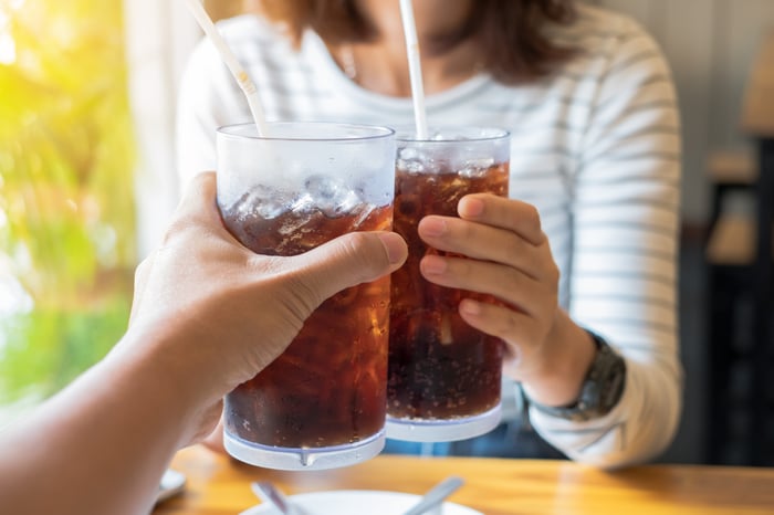 Two people toasting using glasses filled with soda.