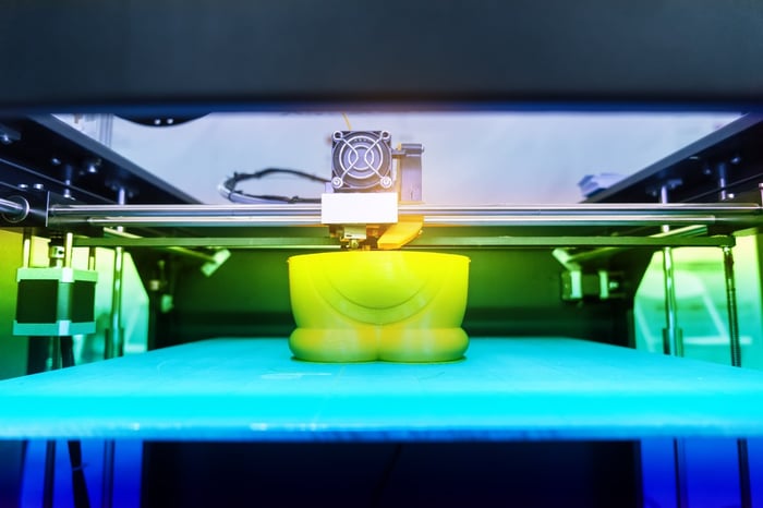 Close-up of a 3D printer producing a bright yellow plastic object.