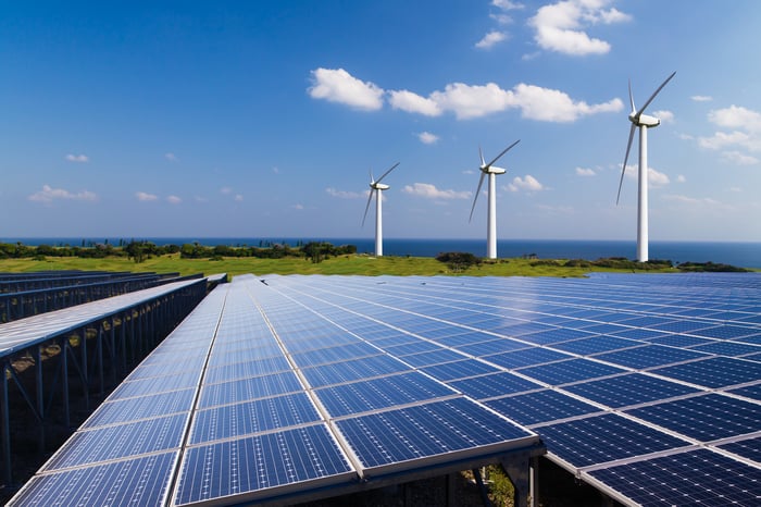 Solar and wind energy farms with body of water in background.