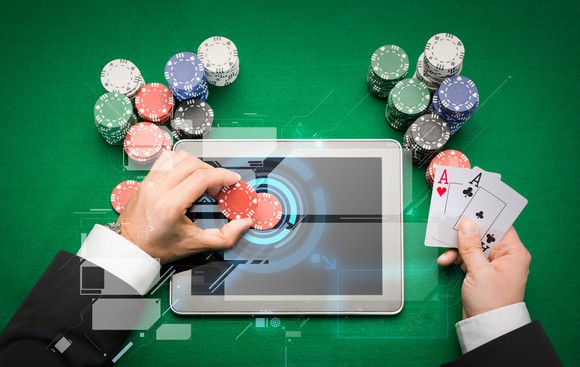 Online casino concept showing a man's hands placing poker chips on a tablet screen, while holding a pair of aces.