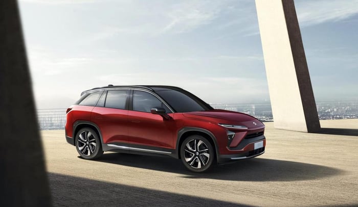 Red NIO electric SUV on a concrete platform, overlooking a city.