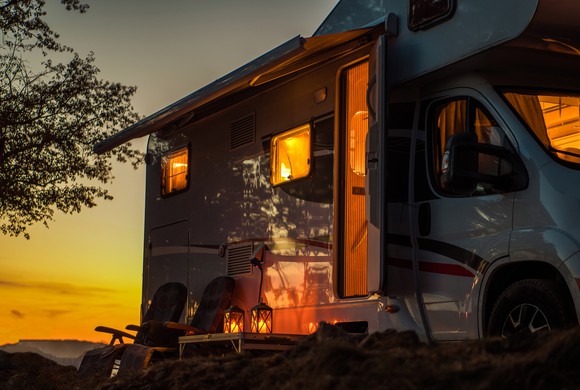 A camper is parked at dusk and warmly illuminated from within.