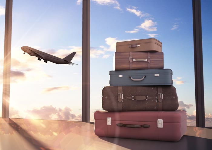 Five suitcases are stacked atop each other, with a plane taking off in the background. 