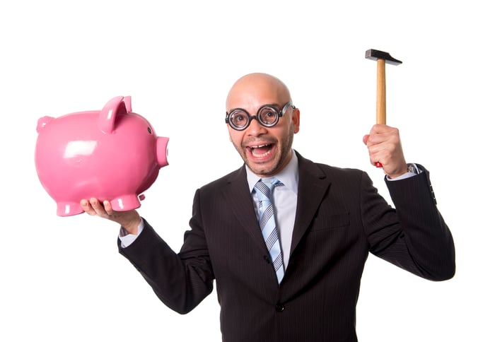 A man in a suit holding a hammer as if he is going to break a piggy bank.