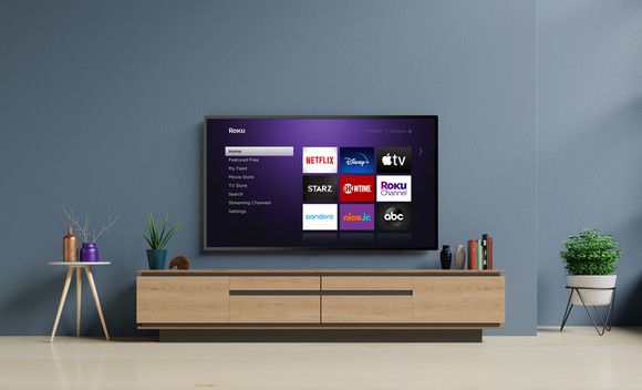 A Roku TV mounted on the wall displaying shortcuts to streaming video channels.