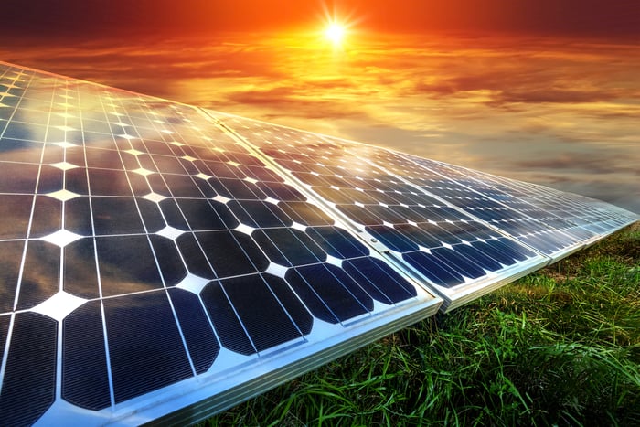 Solar panels on green grass with a bright sun in the background.