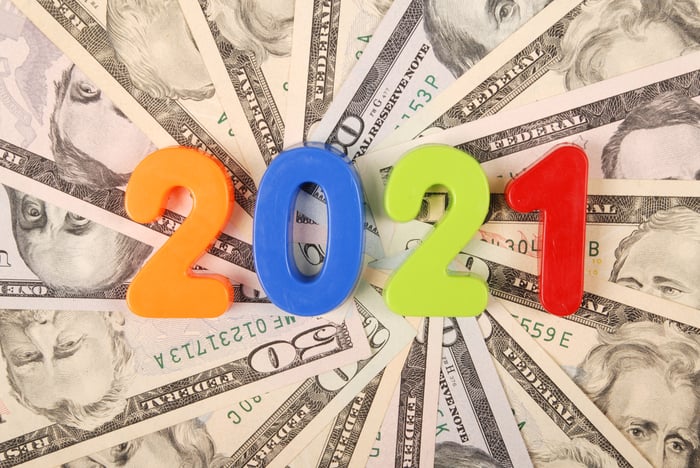 Colored numbers that spell out 2021 lying atop a fanned wheel of cash bills. 