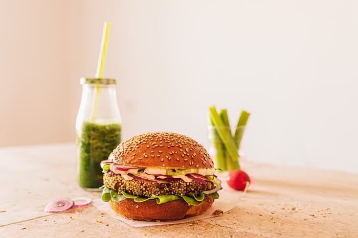 A plant-based burger on a table with a green smoothie nearby. 