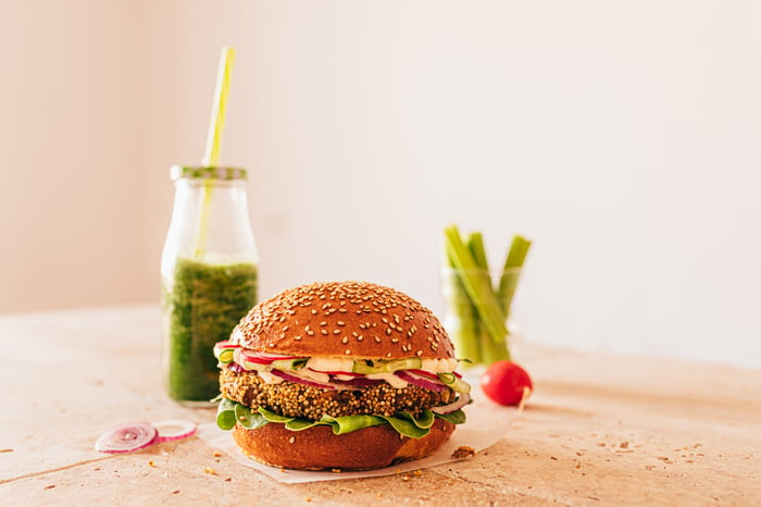 A plant-based burger on a table with a green smoothie nearby. 