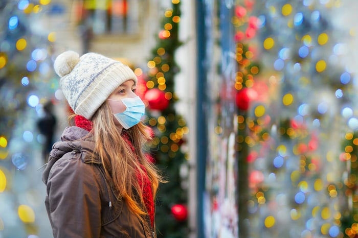 A woman wearing a face mask looks into a window of a store adorned with holiday decorations.