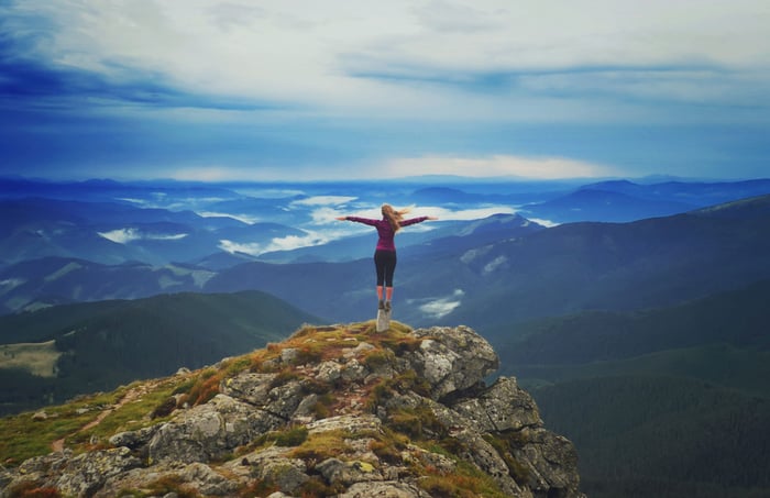 A woman standing on top of a mountain feeling empowered.