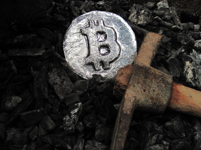 A foil-covered disk displaying the bitcoin symbol sits next to a pickax.