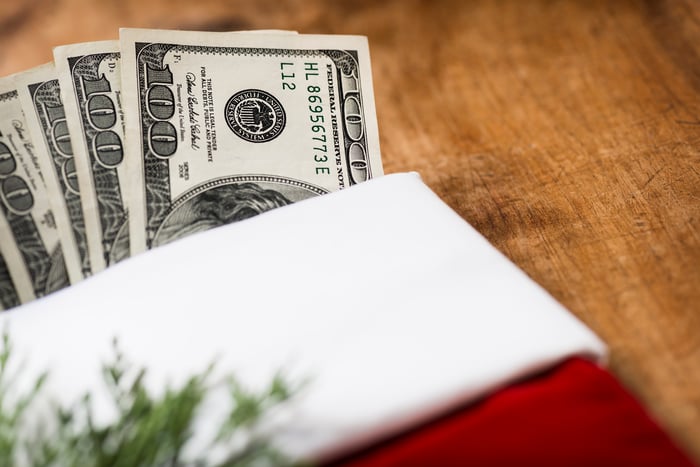 A Christmas stocking lying on a table, with a fanned pile of one hundred dollar bills poking out.