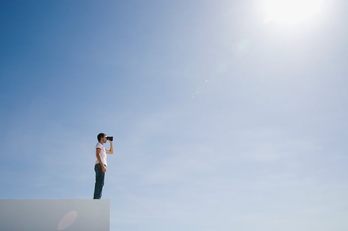 3 Stocks to Buy and Hold for the Next 10 Years 3 Man looking through binoculars under a blue, sunny sky.