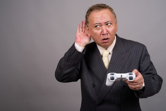 A businessperson holding a video game controller cups his ear and glances sideways.