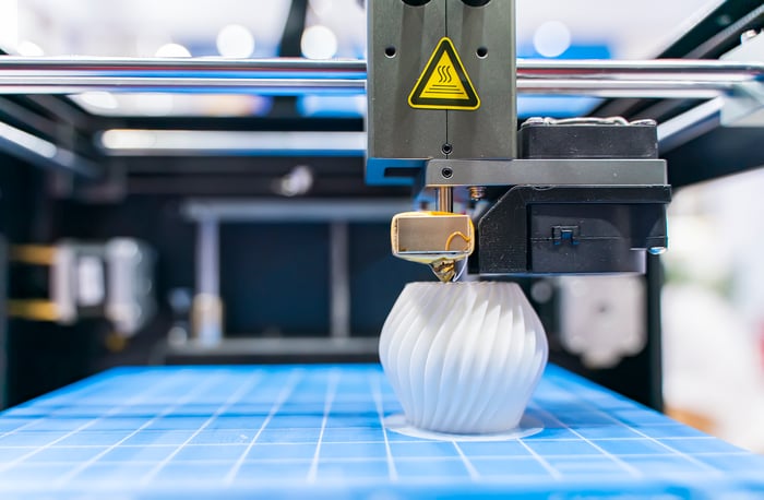 Close-up of a 3D printing producing a white plastic object on a blue surface.