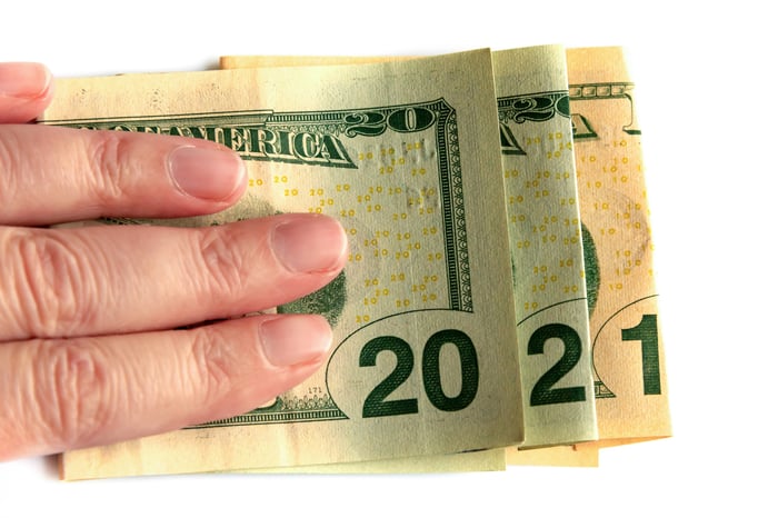 A hand holding cash bills whose denominations spell out 2021.