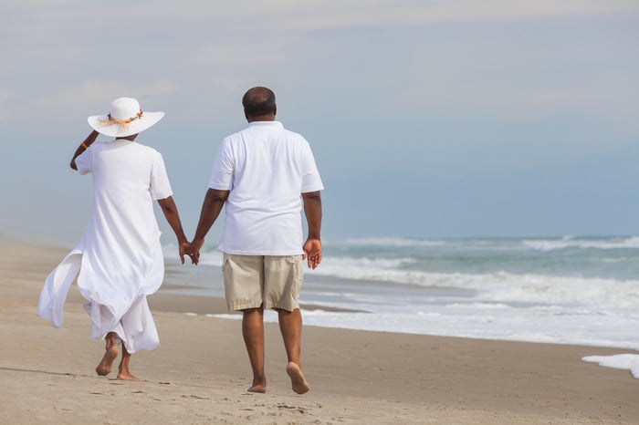 Couple holding hands walking down beach.