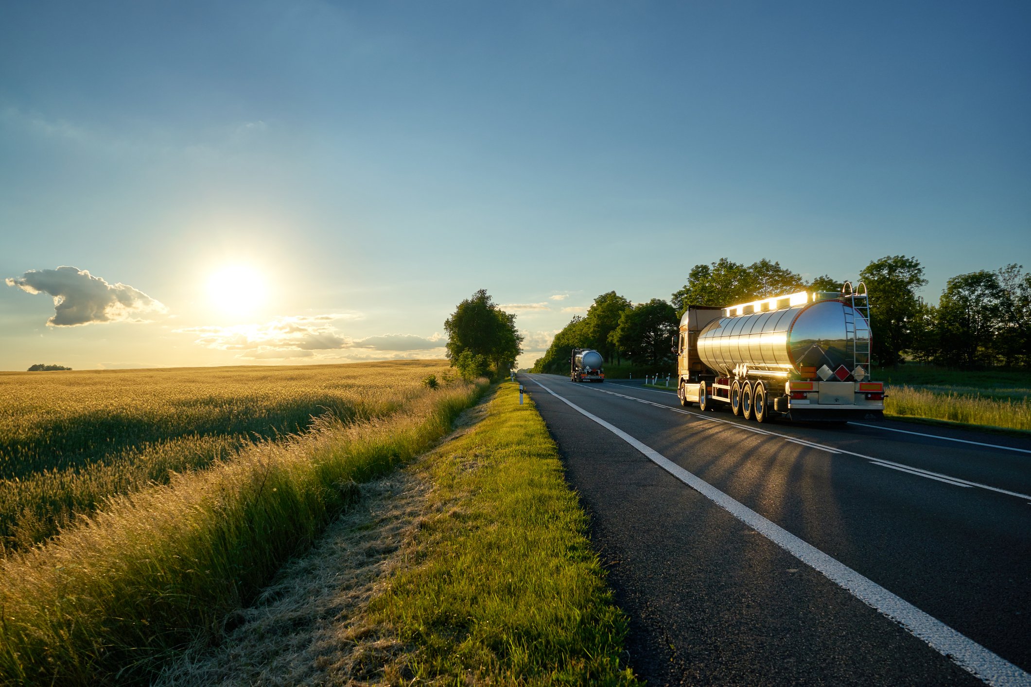 Fuel trucks heading towards the sunset on a country road.