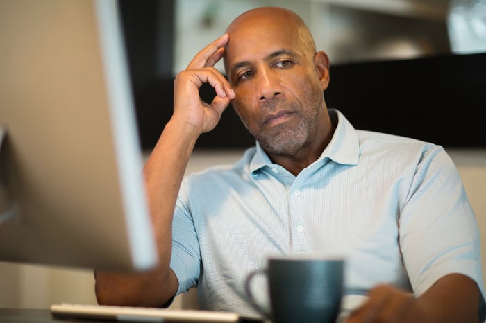 Older man sitting at desk, looking worried.