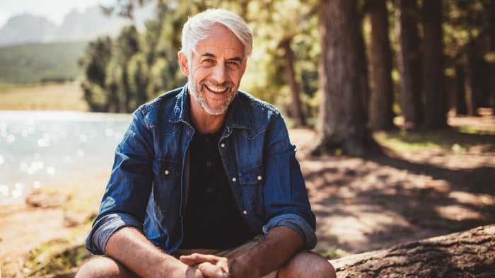 Smiling older man sitting on tree log outdoors