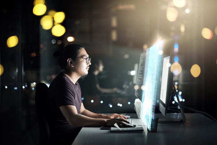 Man coding in a dark room on a computer with a bright screen.