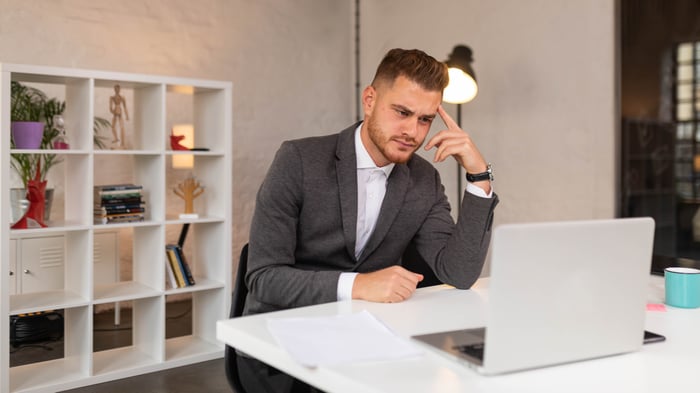 Businessperson at desk looking at laptop with skeptical expression.