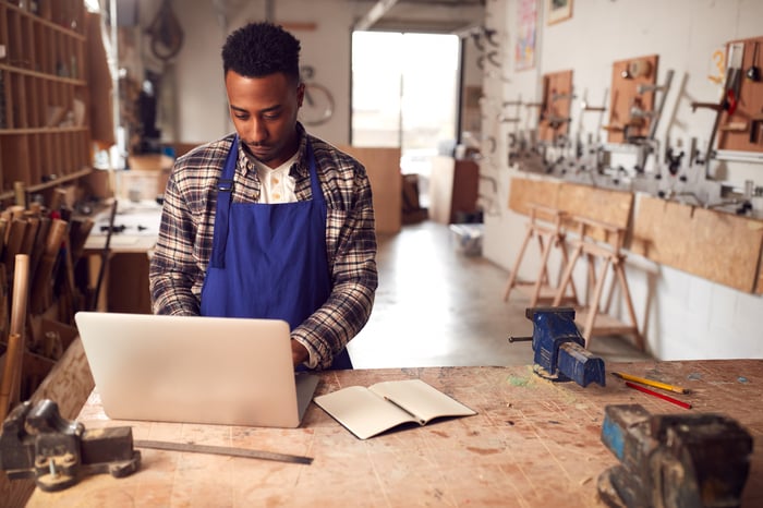 Man in apron in studio typing on laptop