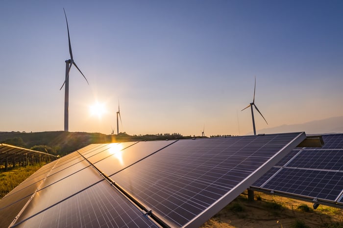 Solar panels and wind turbines in a field at sunrise.