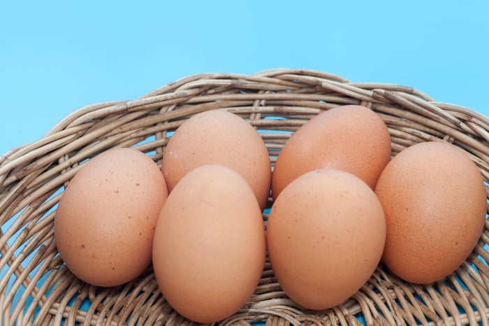 Six brown-shelled eggs in a basket with a blue background.