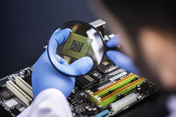 A lab technician examines a semiconductor chip with a magnifying glass.