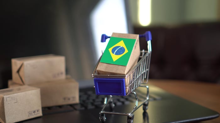 A tiny parcel with a Brazilian flag placed in a cart atop a laptop.