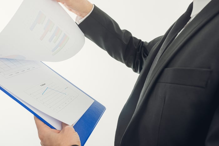 A man in a suit looking over paperwork on a clipboard.