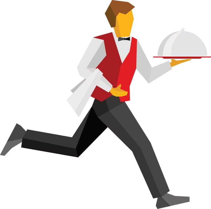 Waiter in red vest running with a covered dish of food.