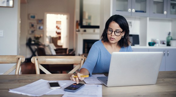 Shot of a young woman using a laptop and calculator while working from home.