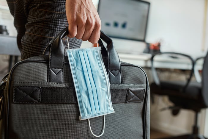 A worker holds a suitcase and a medical mask.