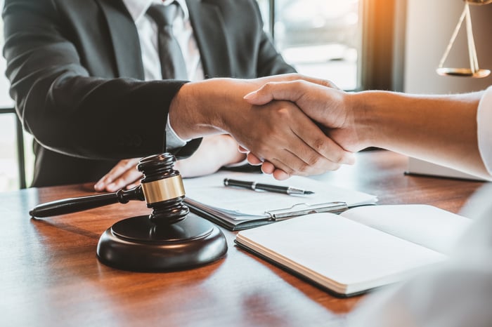 Two lawyers shaking hands over a desk with a gavel and scales in the background