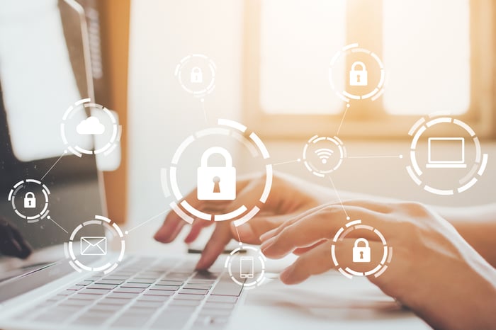 Closeup of hands typing on a computer keyboard while a padlock icon floats in the foreground surrounded by other computer icons.