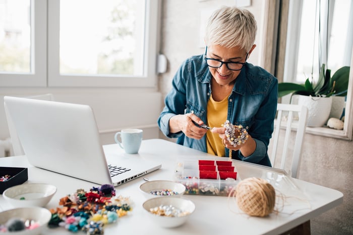 A woman making crafts in front of a computer.