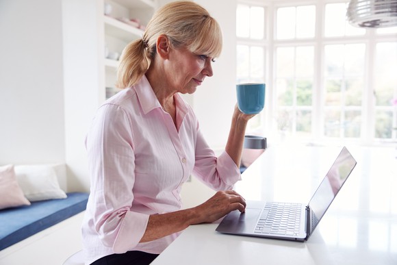 Older woman at laptop holding mug