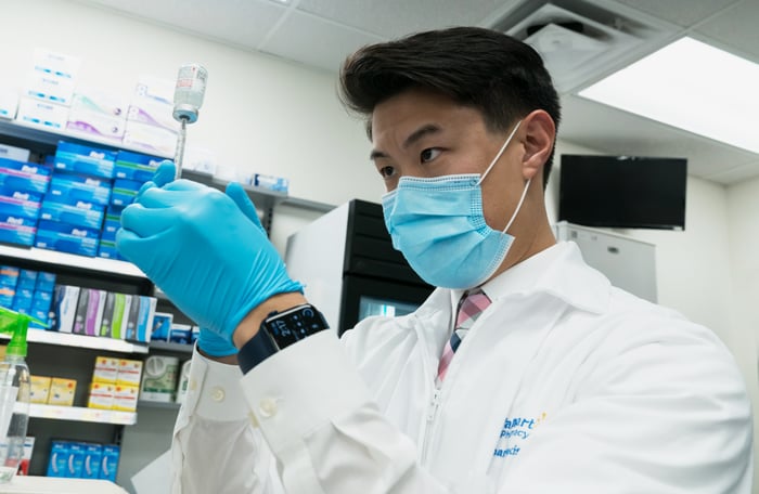 Walmart pharmacist inserting a needle in a vaccine bottle.