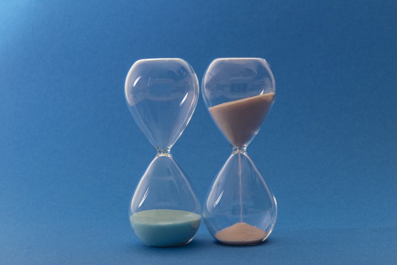 An hourglass with all of its sand at the bottom next to another hourglass with most of the sand still in the top half