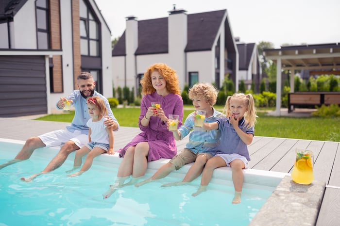 A family drinking lemonade at a pool behind a house.