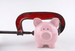 Clamp squeezing a piggy bank -- GettyImages-477424223