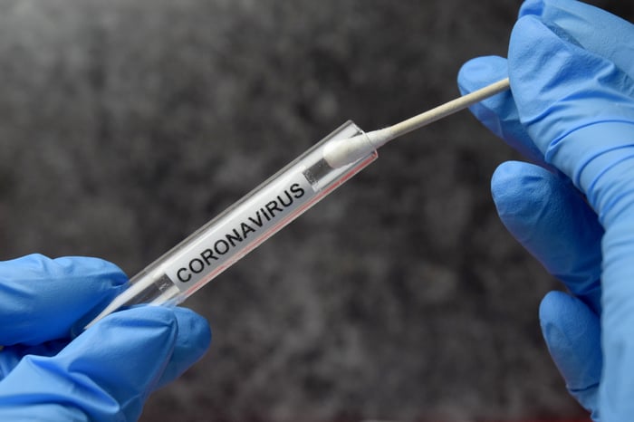 A gloved scientist holding a cotton swab and a glass vial marked coronavirus. 